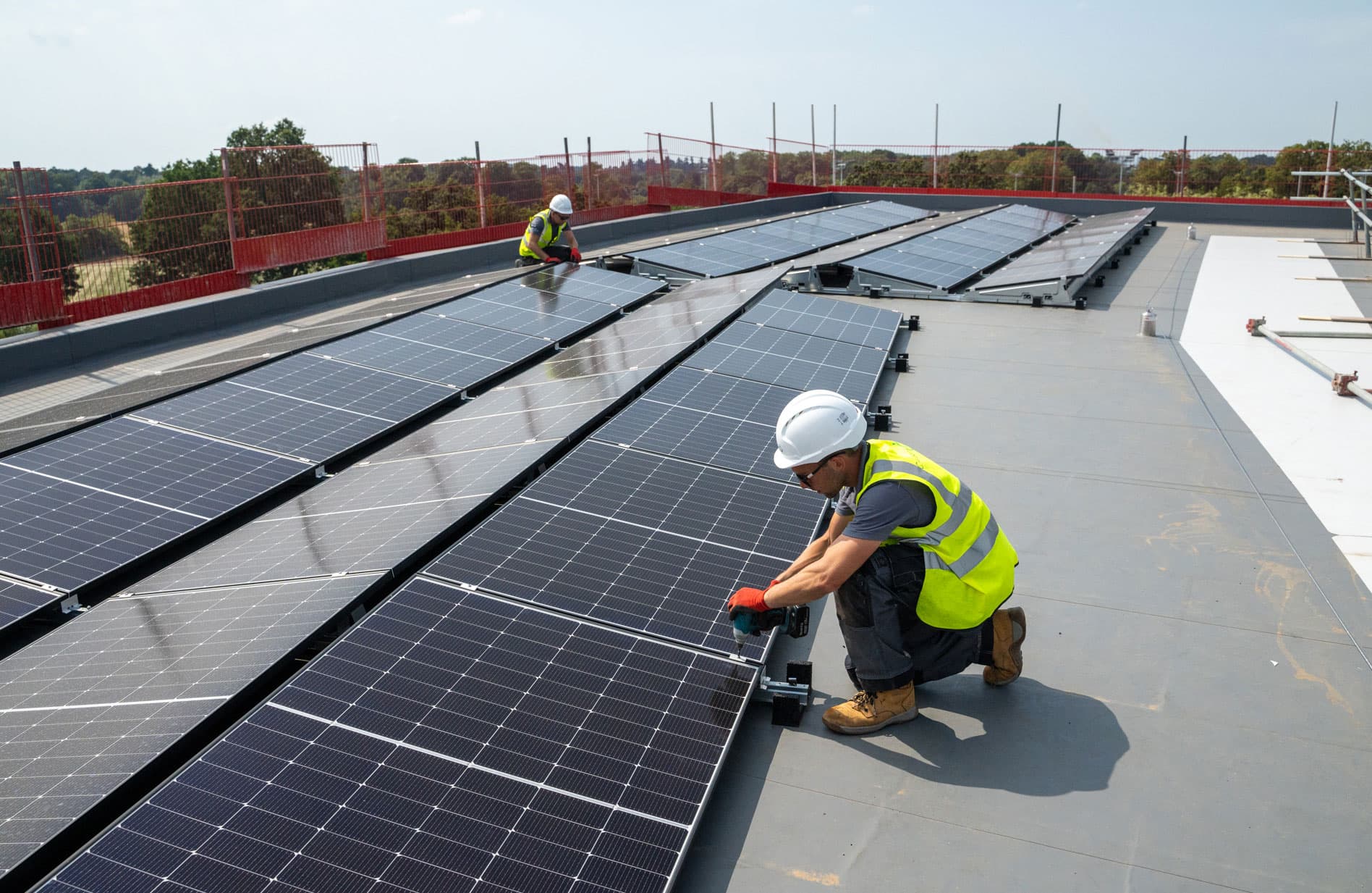 Two Utilita Business engineers installing solar panels on a commercial rooftop, supporting clean energy solutions in UK sport.