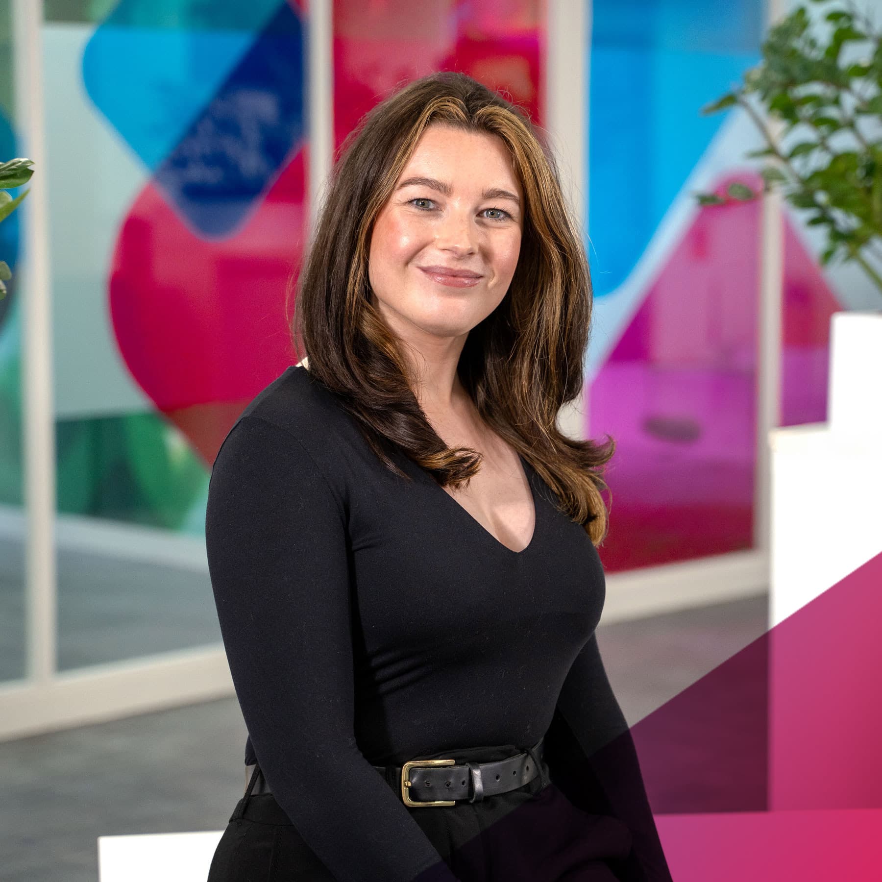 Mid-shot of Ella Moorey, Group Sustainability Lead at Utilita, sat in an office with colourful glass panels in the background.