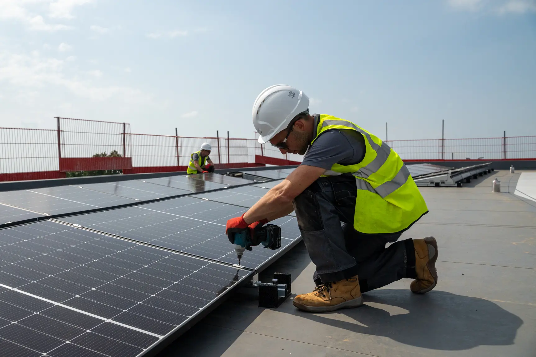 Two Utilita Business engineers installing solar panels on a commercial rooftop, supporting clean energy solutions in UK sport.
