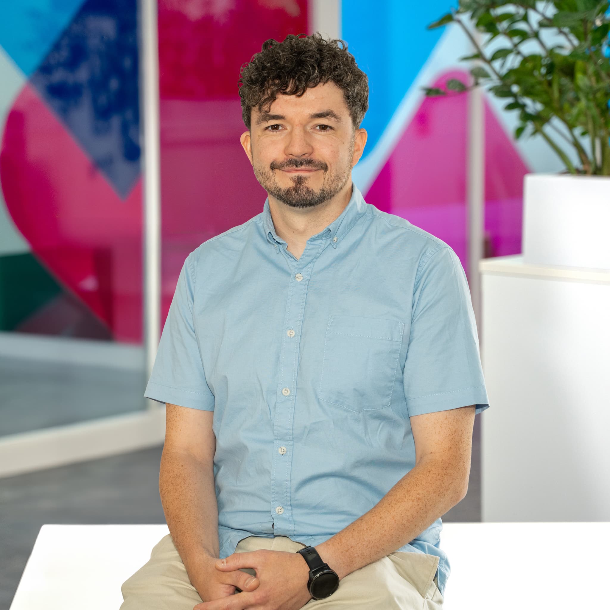 Photo of Andrew Flynn, Commercial Sales Mentor at Utilita Business, sat in front of colourful glass panels.
