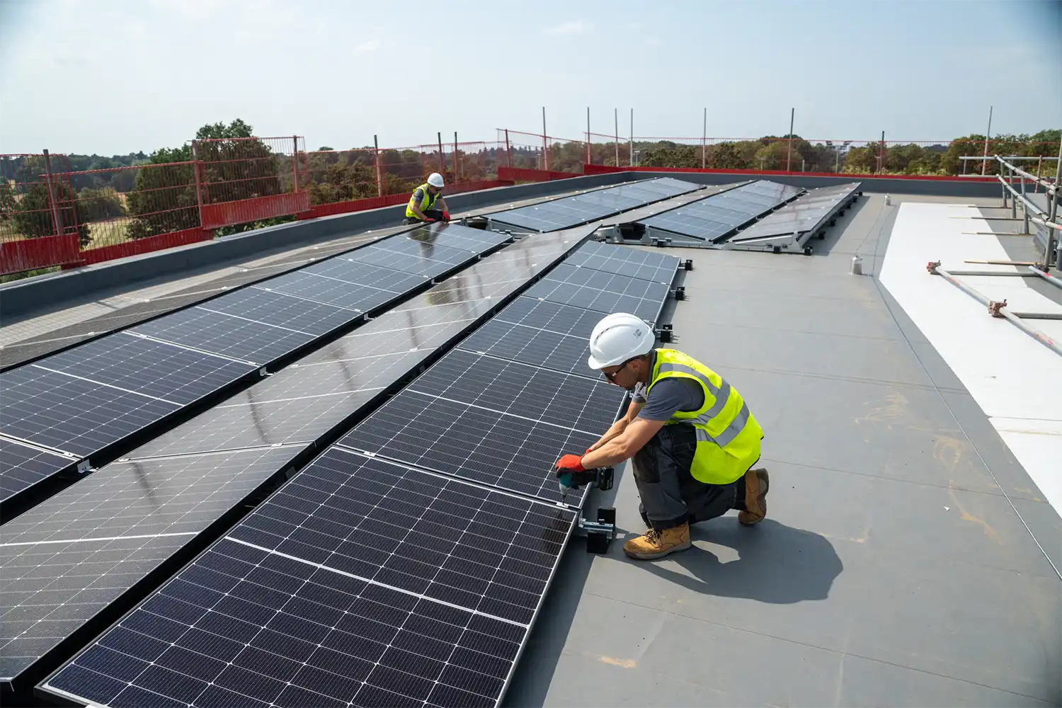 Two Utilita Business engineers installing solar panels on a commercial rooftop, supporting clean energy solutions in UK sport.