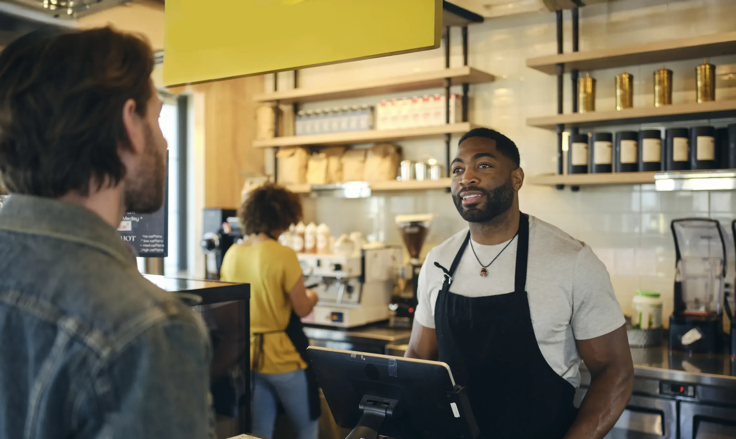Image of a cafe employee working in a small business, taking a customer's drink order at the till.